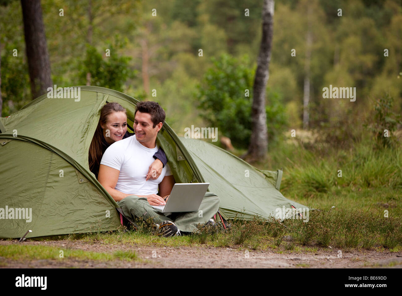 Una pareja utilizando un ordenador fuera de una tienda de campaña en un camping Foto de stock