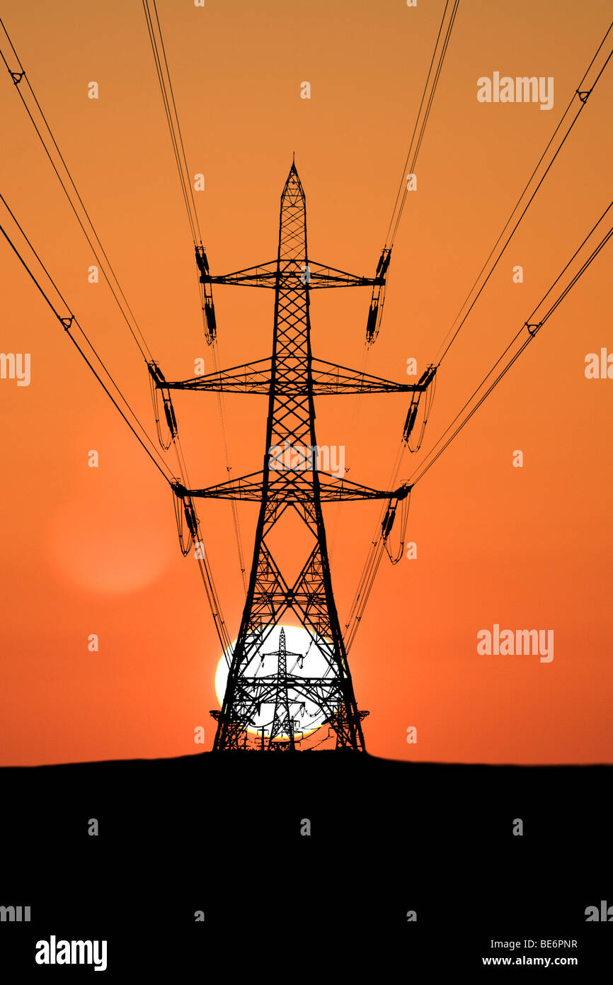 Línea de torres de alta tensión y puesta de sol Foto de stock