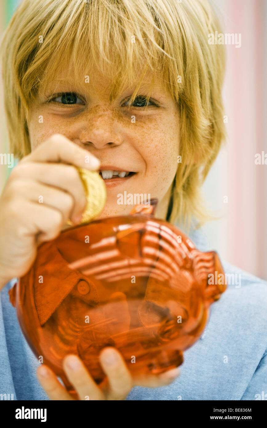 Boy colocando una moneda en la hucha Foto de stock
