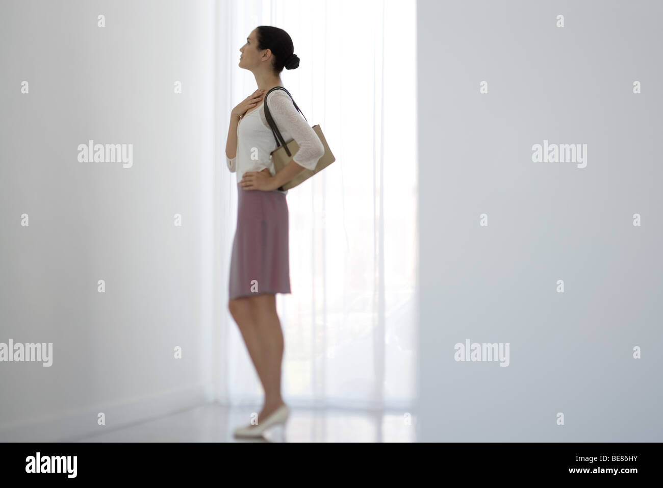Mujer de pie junto a la ventana, mirando hacia arriba, vista lateral Foto de stock