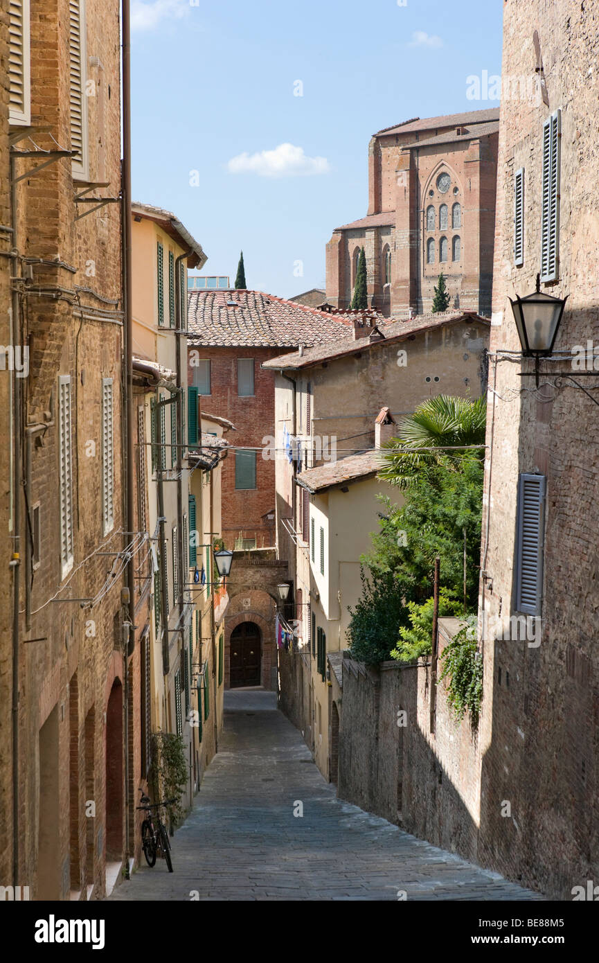 Estrecho callejón en el casco antiguo con la iglesia de San Domenico detrás, Siena, Toscana, Italia Foto de stock