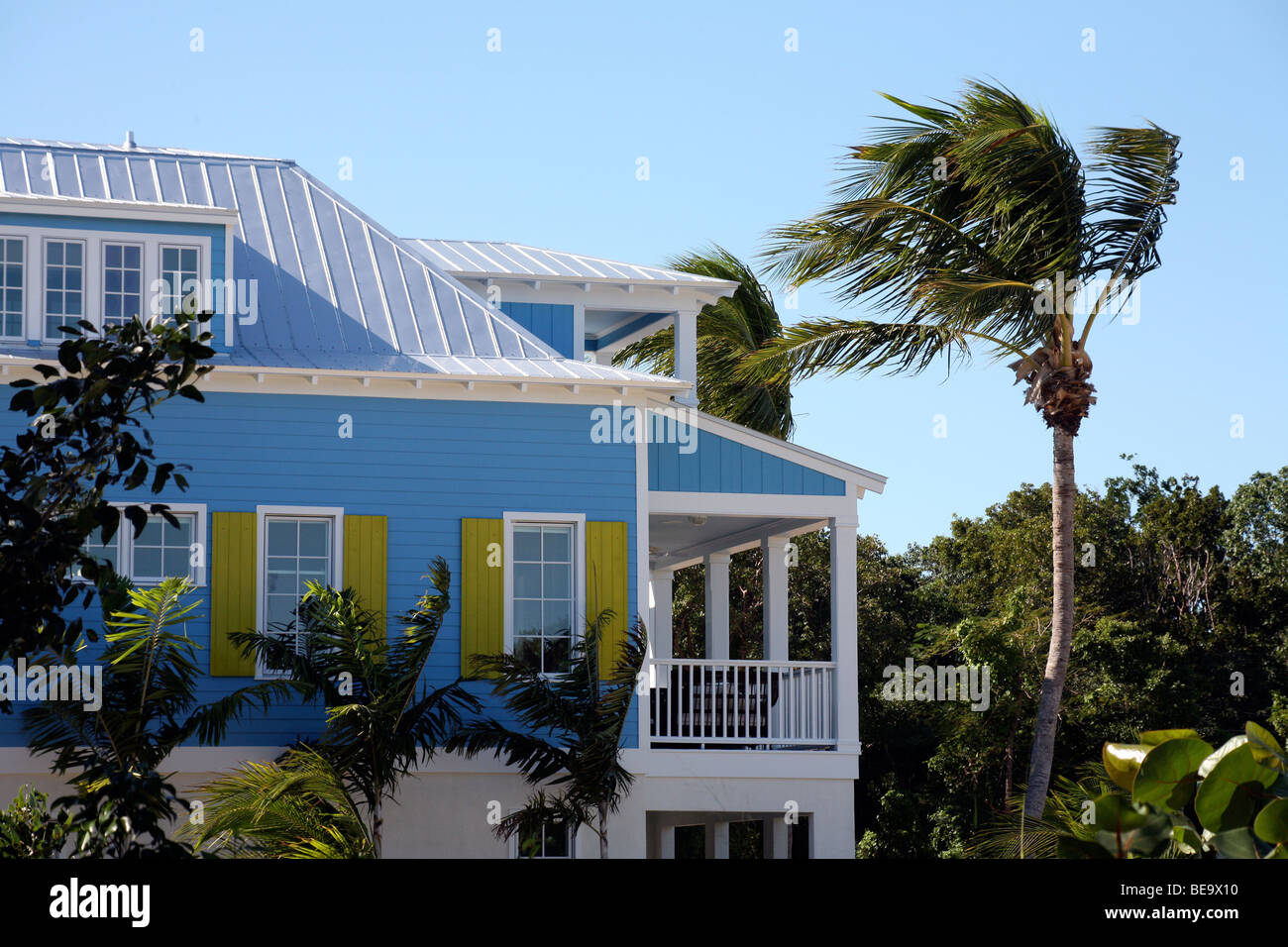 Casa Tropical de azul y blanco, con persianas de color amarillo y una veranda blanco entre palmeras contra un cielo azul Foto de stock