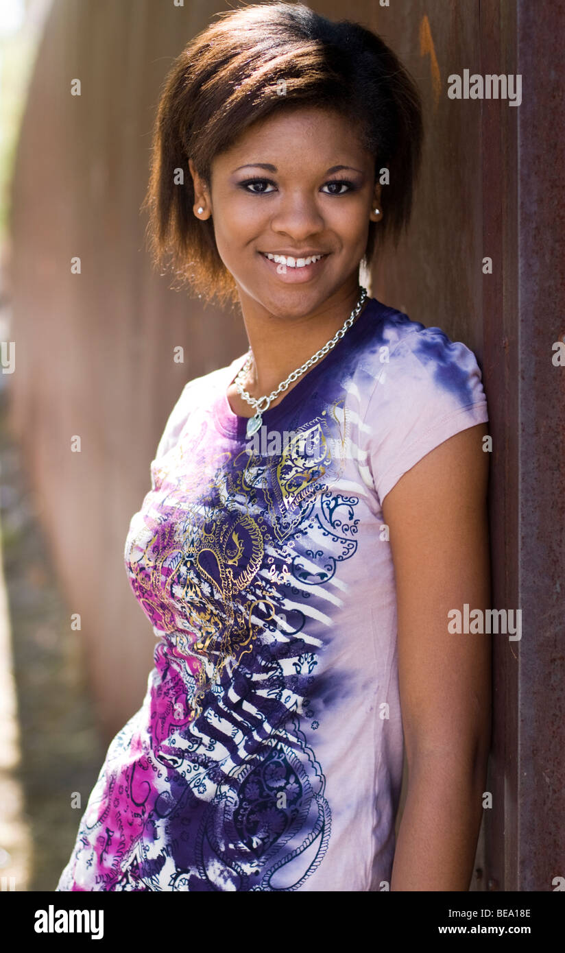 Una joven chica Afroamericana está apoyada en una pared y sonriente Foto de stock