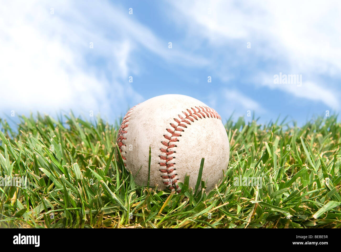 Una pelota de béisbol acostado en un campo de hierba verde con un hermoso cielo. Foto de stock