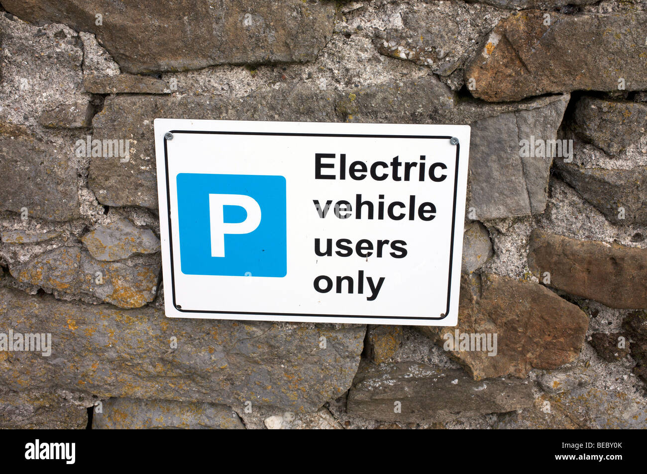 Azul y blanco, señal de estacionamiento para vehículos eléctricos fijados a una pared de piedra caliza Foto de stock