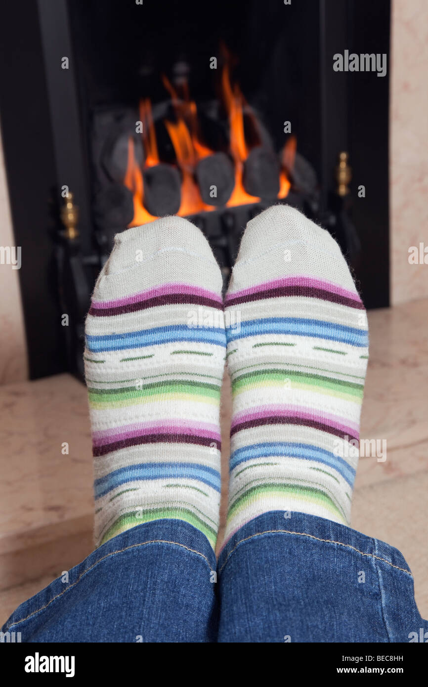 Cerca de un par de fríos en acogedores calcetines de lana de rayas calentándose frente a un de carbón en una chimenea en casa en invierno. REINO UNIDO Fotografía