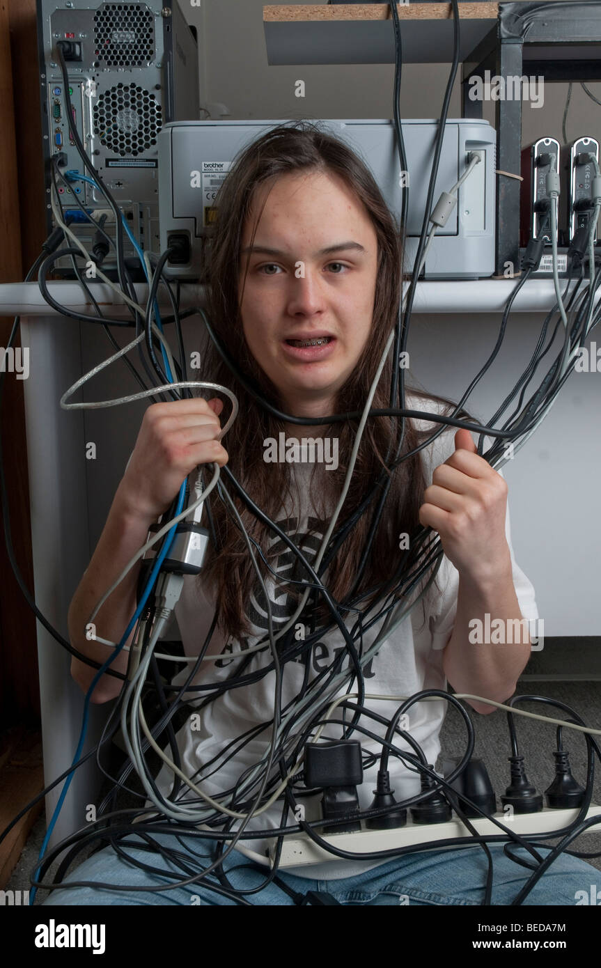 Adolescente de pelo largo enredado en cables de computadora Foto de stock