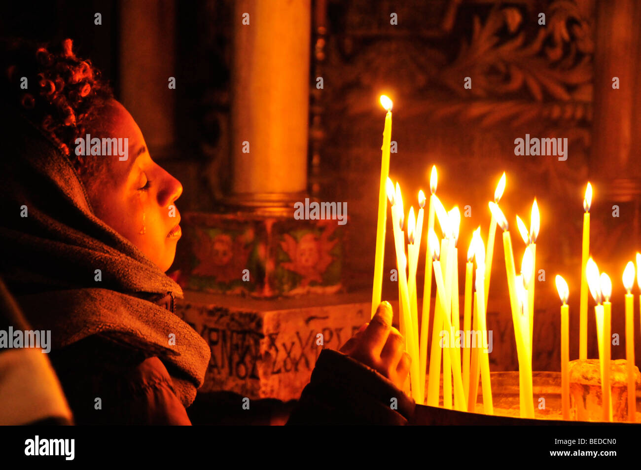 Joven creyente con lágrimas en los ojos encendiendo una vela en la tumba de Cristo en la Iglesia del Santo Sepulcro, de Jerusalén, Foto de stock