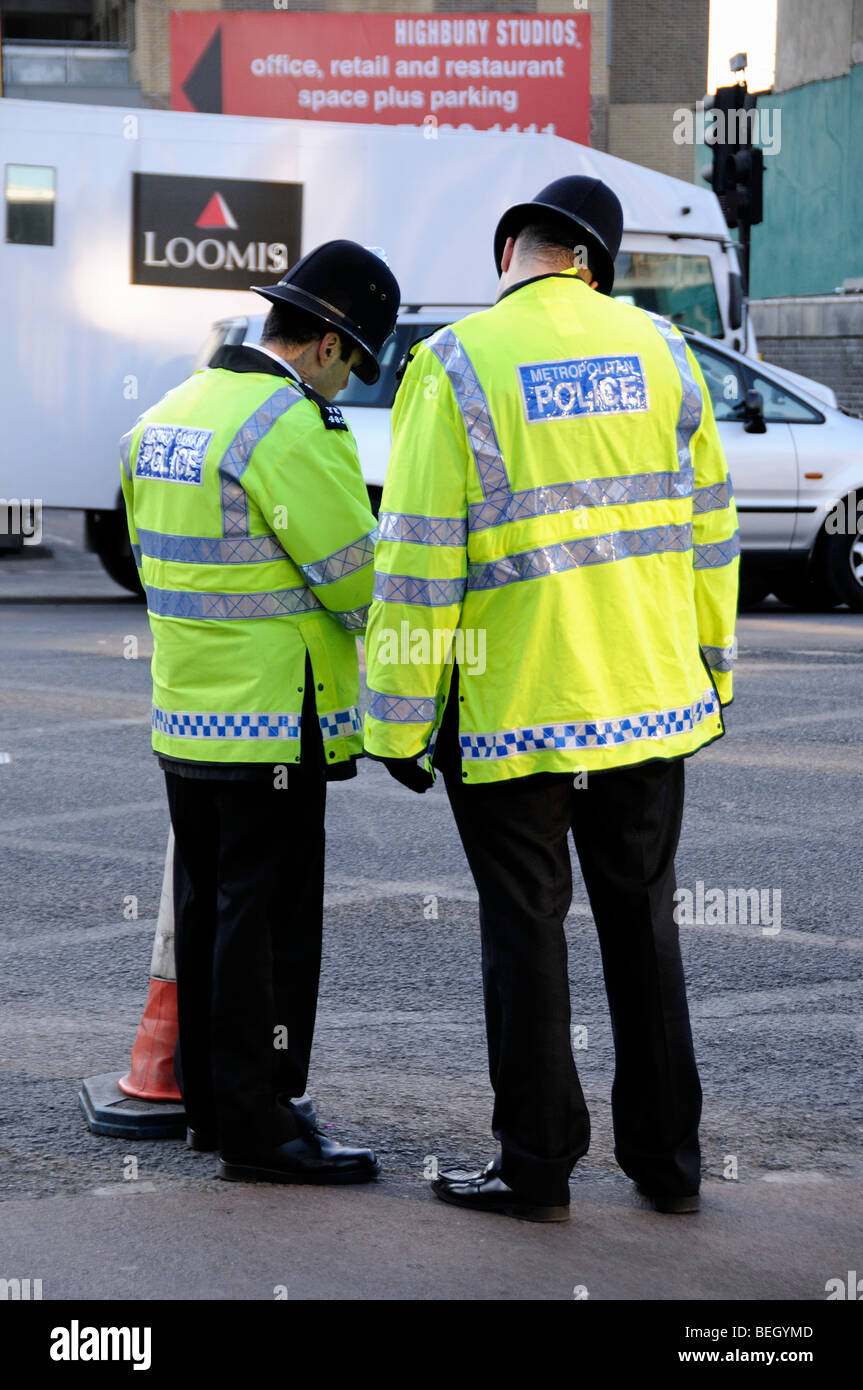 Dos funcionarios de la Policía Metropolitana en amarillo chalecos reflectantes de pie en Holloway Road Londres England Reino Unido Foto de stock