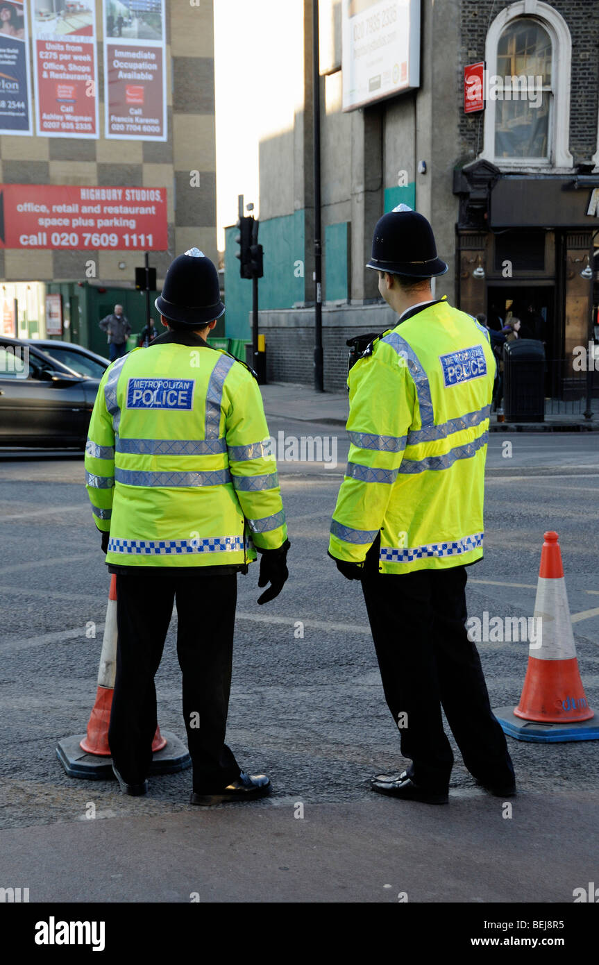 Dos funcionarios de la Policía Metropolitana por detrás con conos de tráfico en Holloway Road Londres England Reino Unido Foto de stock