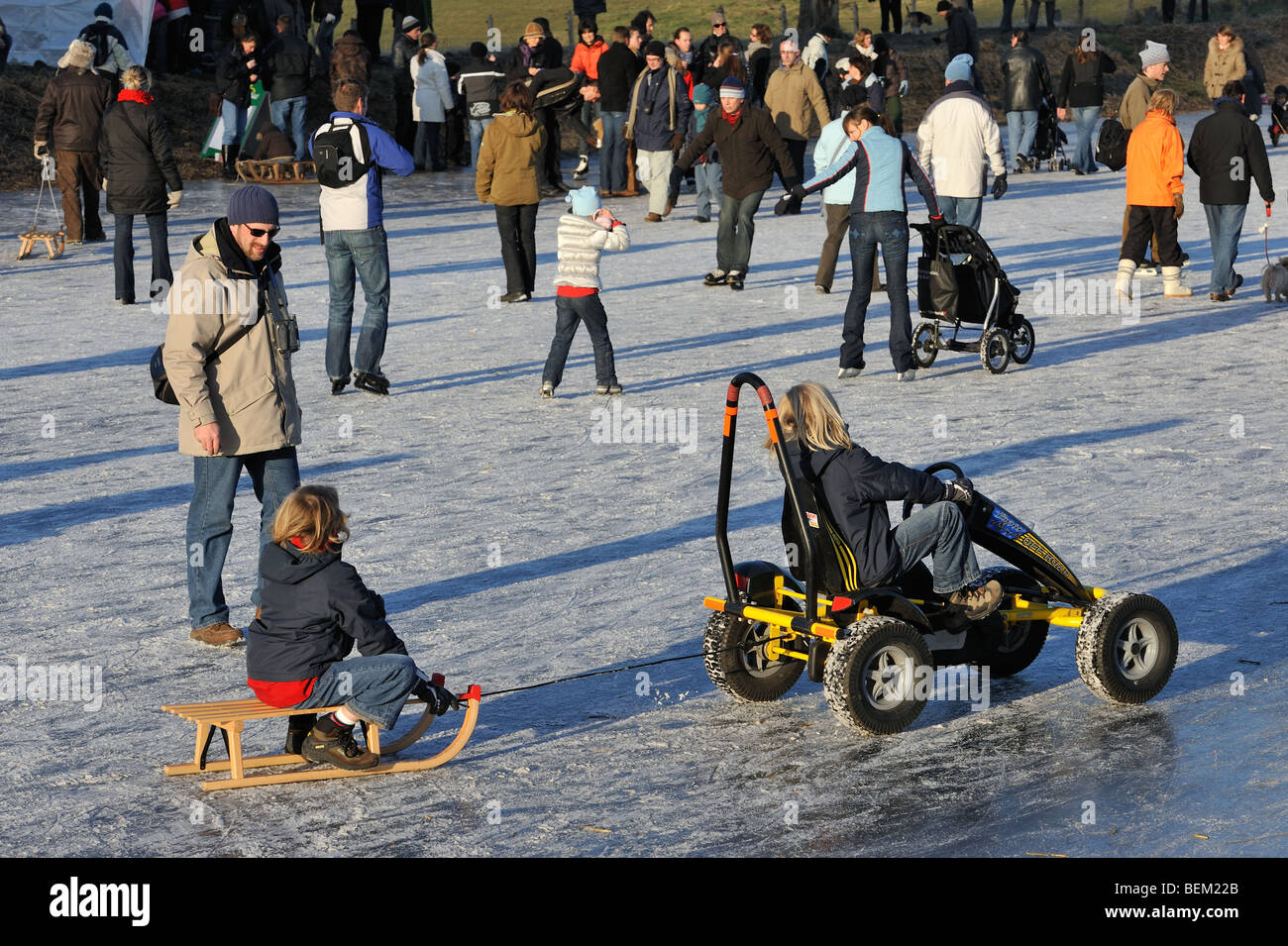 Niño en trineo tirado por go-cart entre los patinadores sobre hielo patinaje sobre hielo de río congelado en invierno Foto de stock