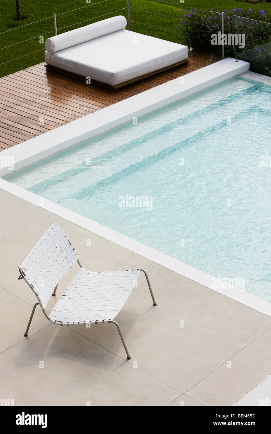 Silla en el borde de la piscina, tomar el sol en la cubierta de la cama en segundo plano. Foto de stock