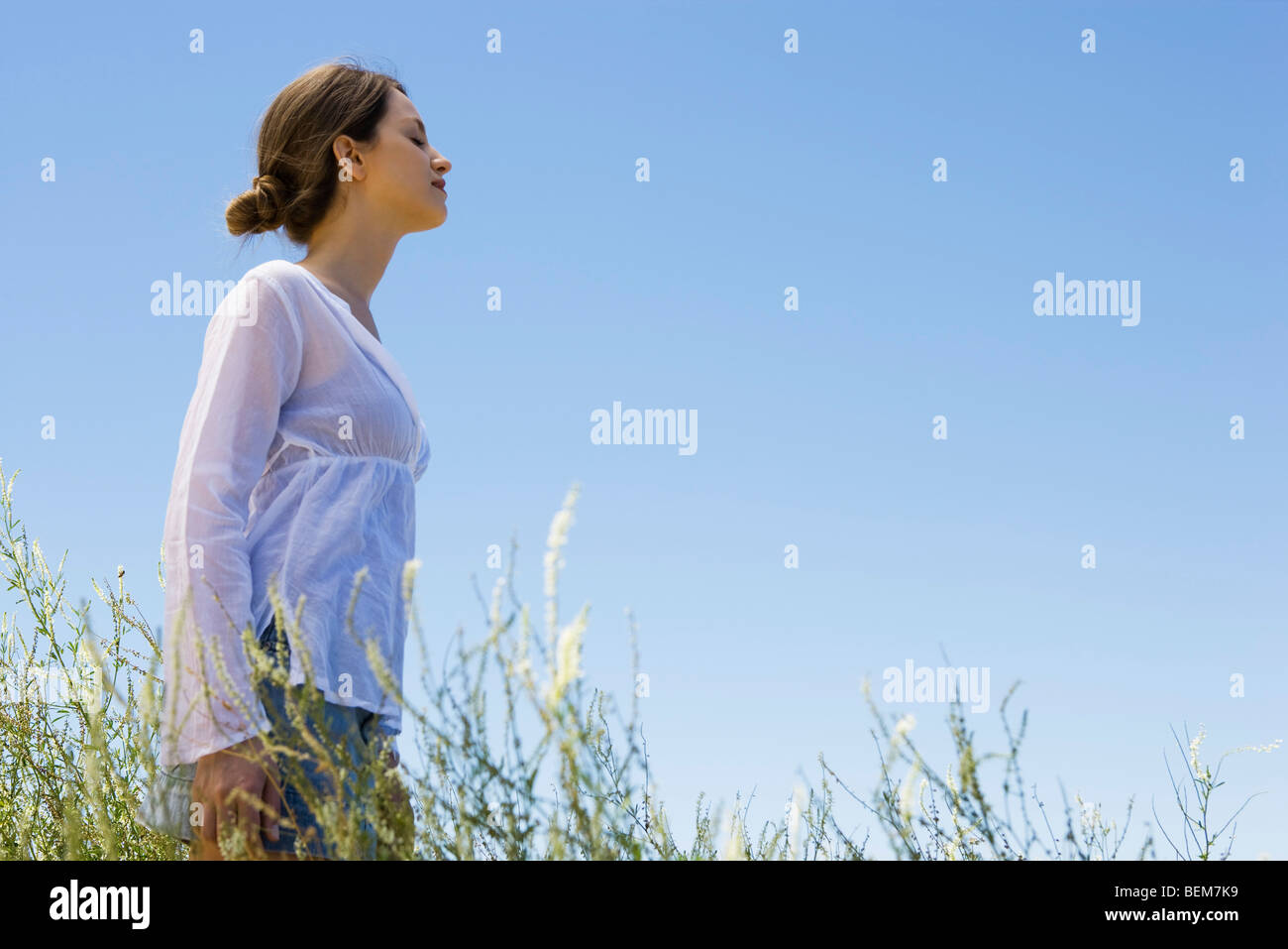 Mujer joven de pie en el pasto alto con los ojos cerrados, vista lateral Foto de stock