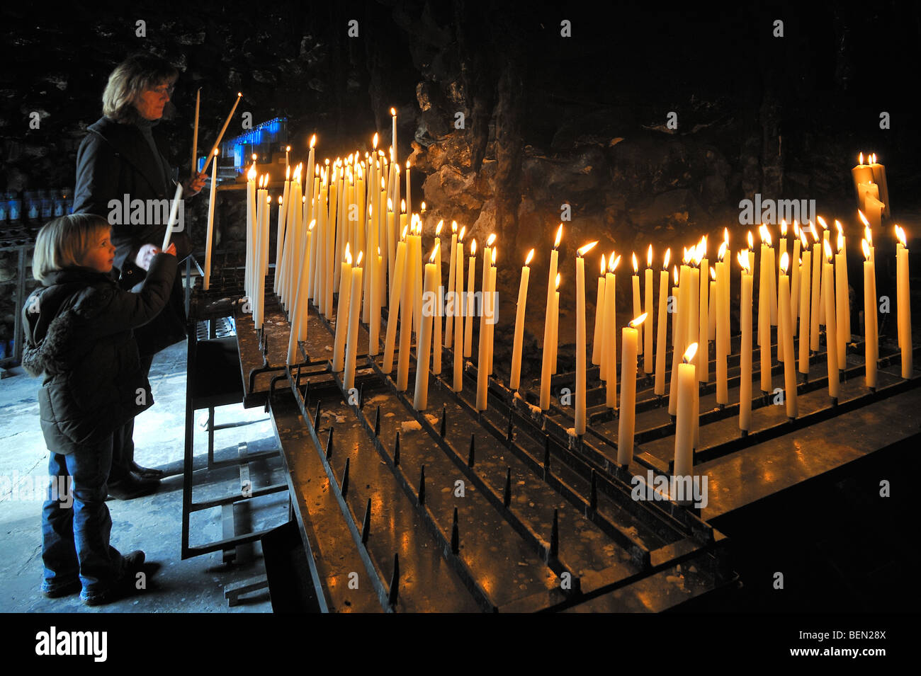 Madre e hijo encendiendo velas y rezando en la gruta de Lourdes, lugar de peregrinación Oostakker-Lourdes, Flandes, Bélgica Foto de stock