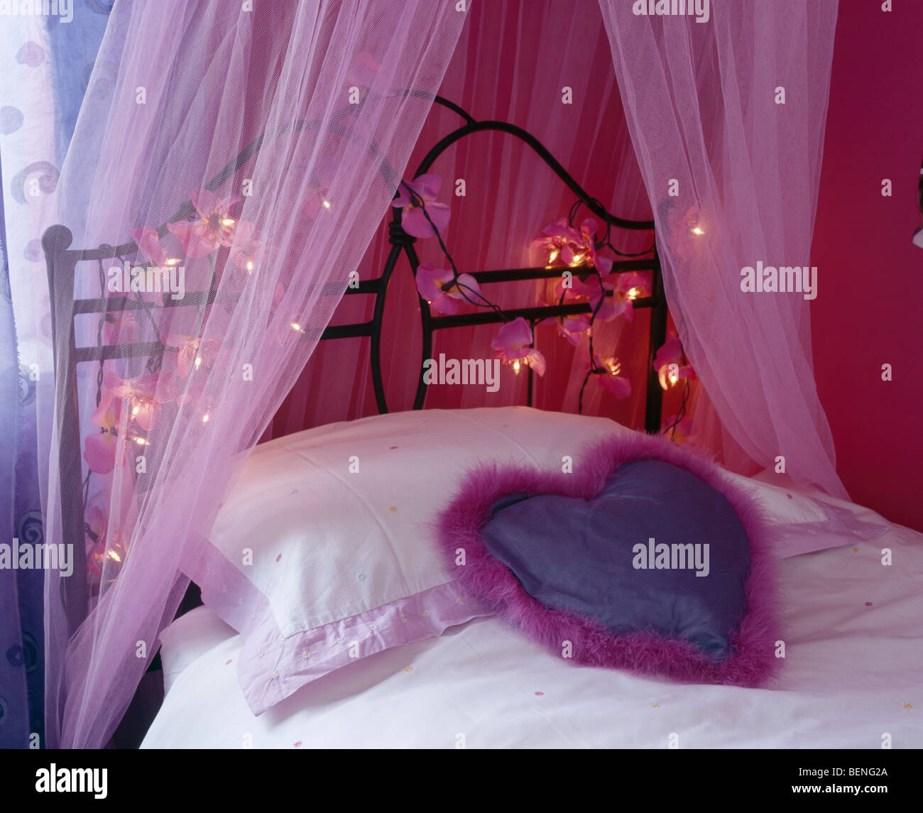 Close-up de cojín con forma de corazón en metal cama individual con  cortinas de voile rosa alrededor de la cabecera de la cama vestidas con las  luces de hadas Fotografía de stock -