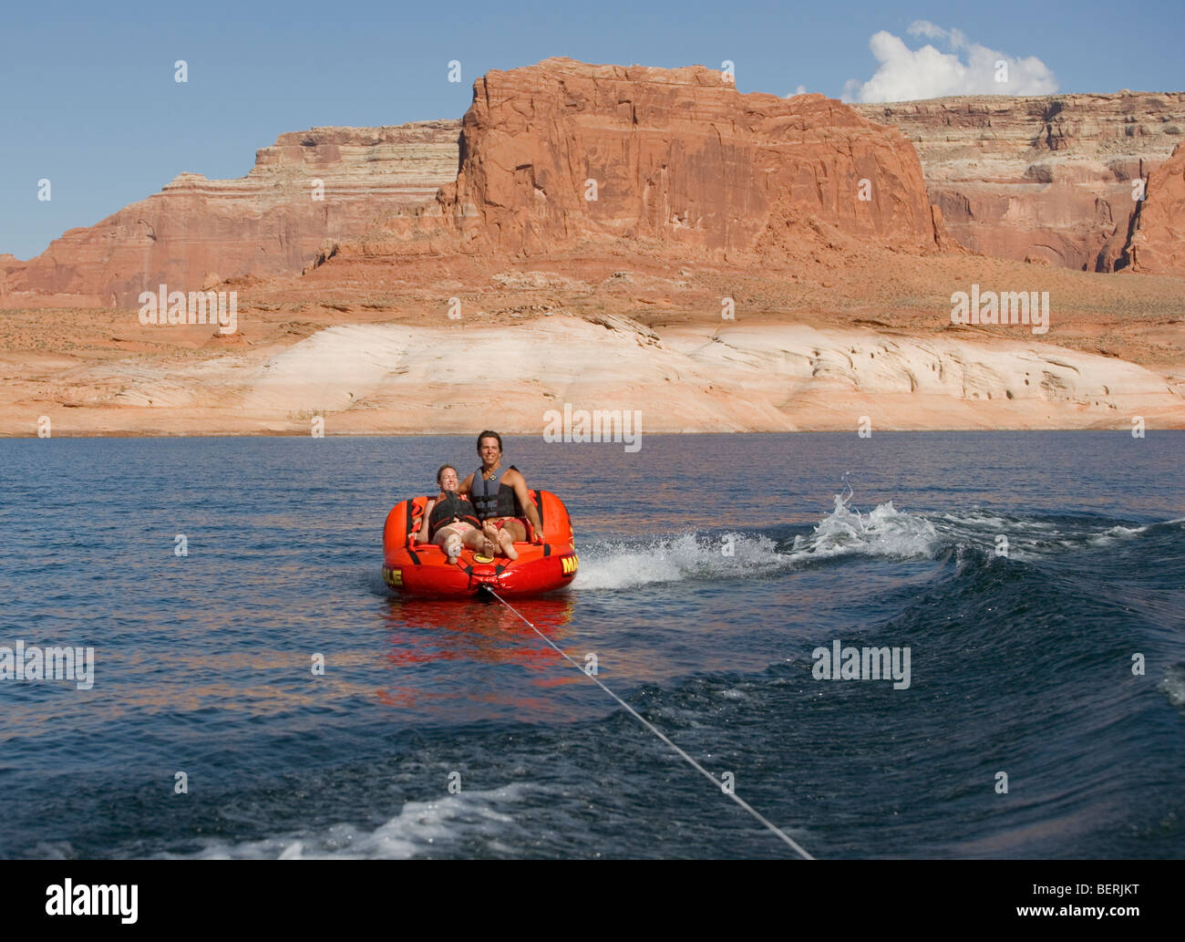 Una pareja se monta sobre un remolque hinchable mientras es remolcado detrás de un bote en el lago Powell, en Utah, EE.UU.. Foto de stock
