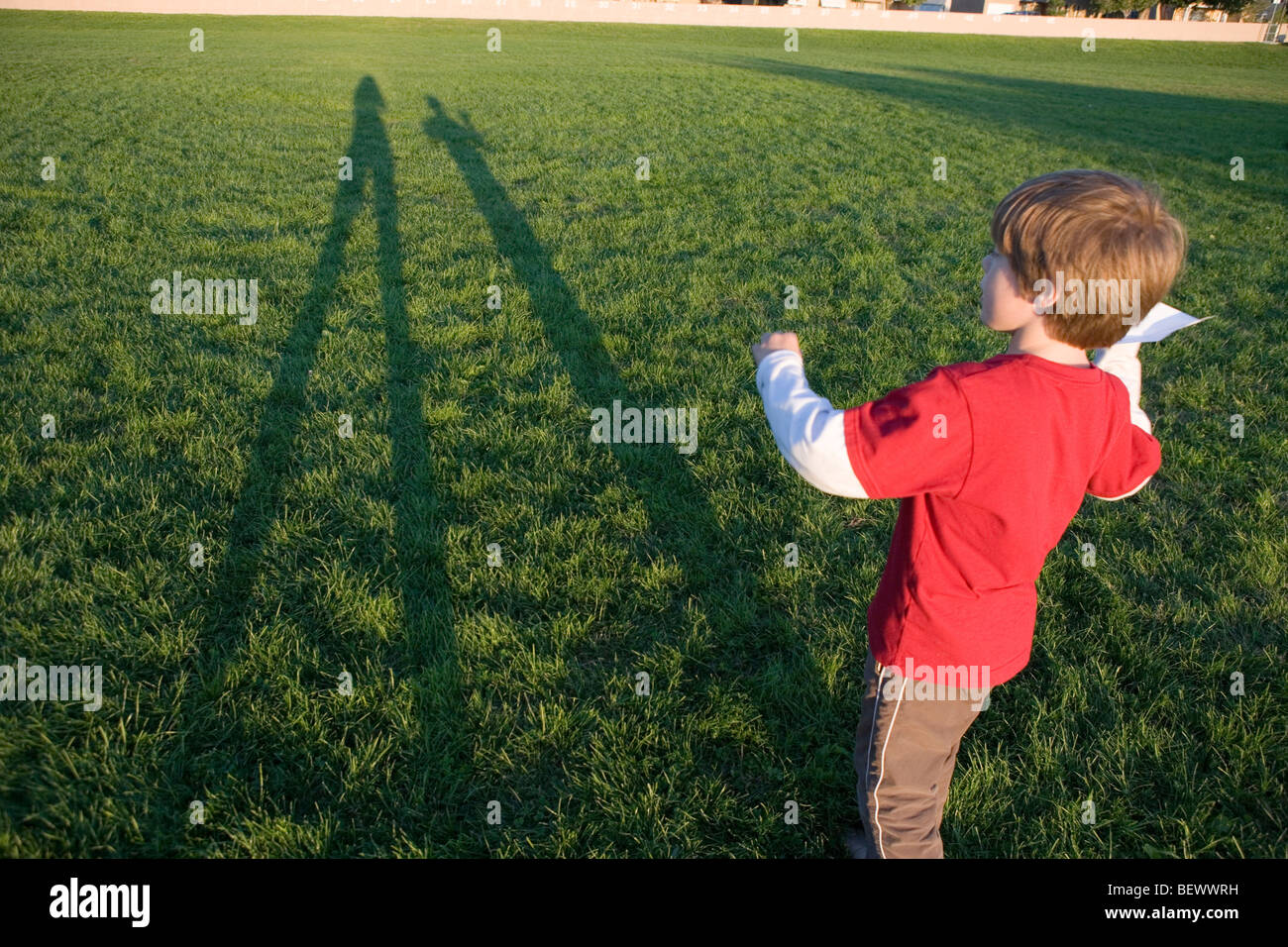 Niño de siete años preparándose para lanzar un avión de papel en un campo abierto Foto de stock