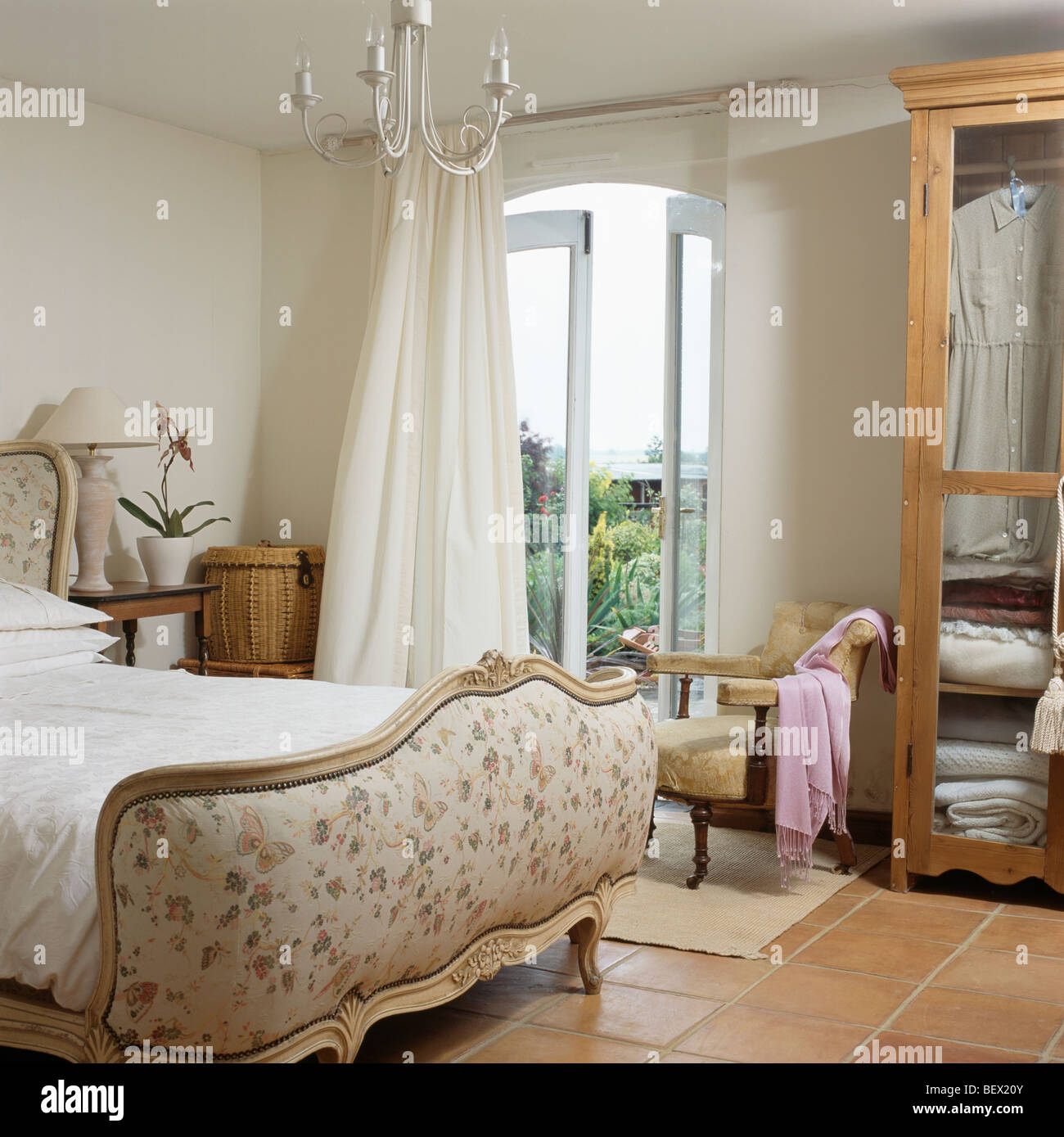 Cama francesa tapizados en crema crema país dormitorio con las cortinas a  ventanas francesas con vistas al jardín Fotografía de stock - Alamy