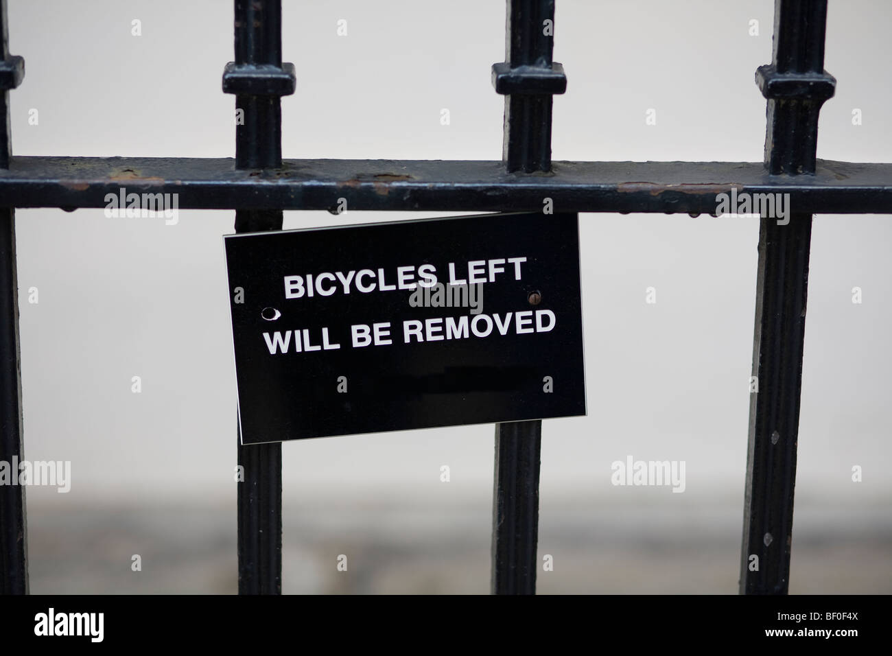 Escritura blanca, "bicicletas izquierda será retirado", en signo de negro sobre negro colgado barandas de hierro forjado. Londres, Reino Unido. Foto de stock