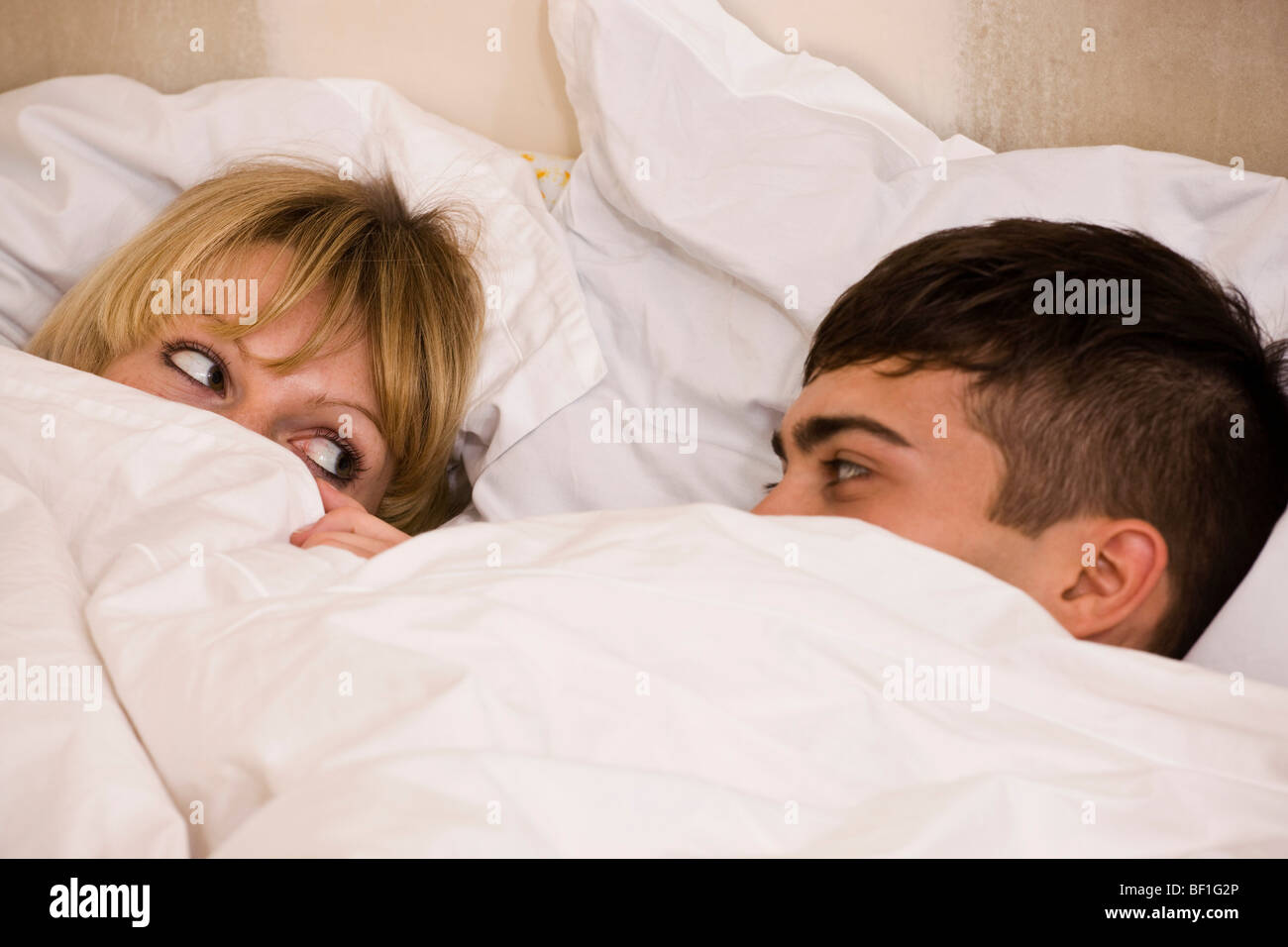 Una joven pareja en la cama con el edredón tirado a sus ojos Foto de stock