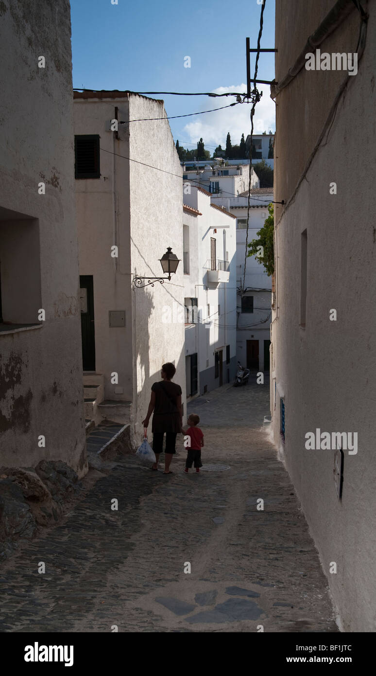 Una madre camina a su hijo hacia abajo las empedradas callejuelas del norte de España, una tarde de sol golpea el anciano paredes blancas. Foto de stock