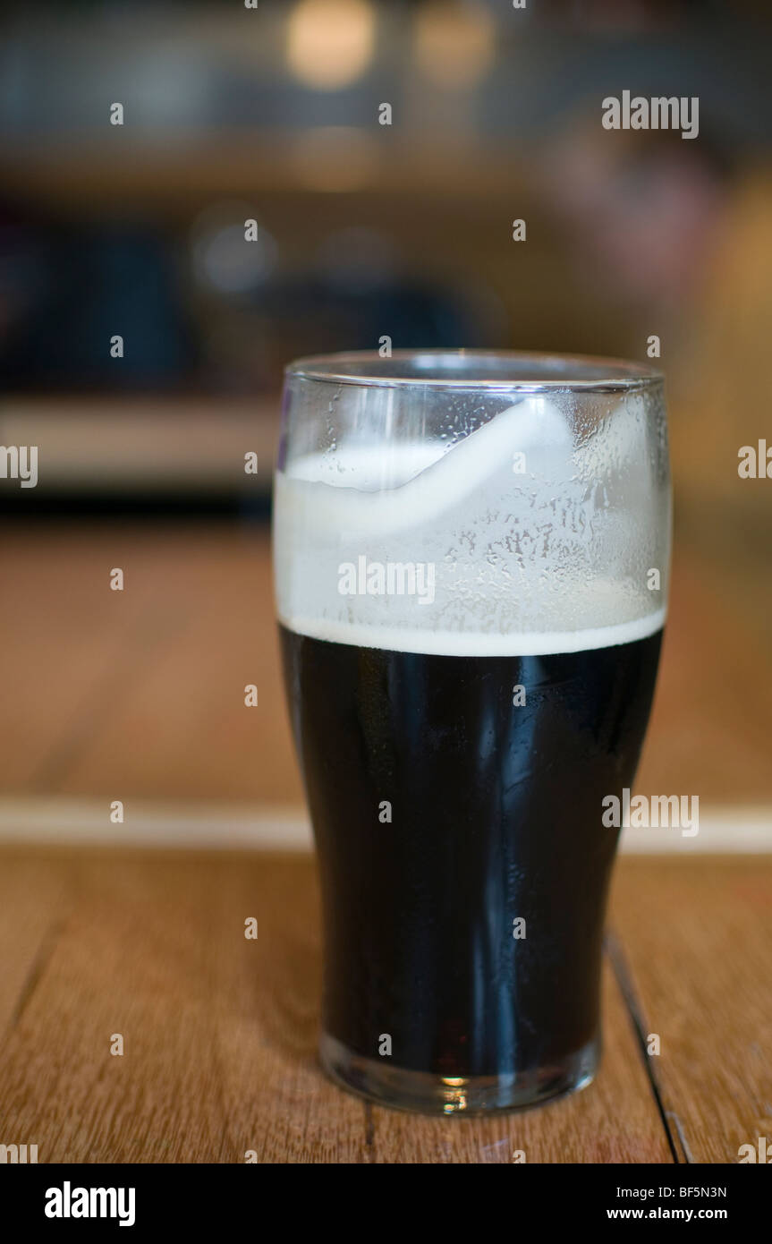 Una pinta de cerveza negra real ale sentado en una mesa de pub Foto de stock