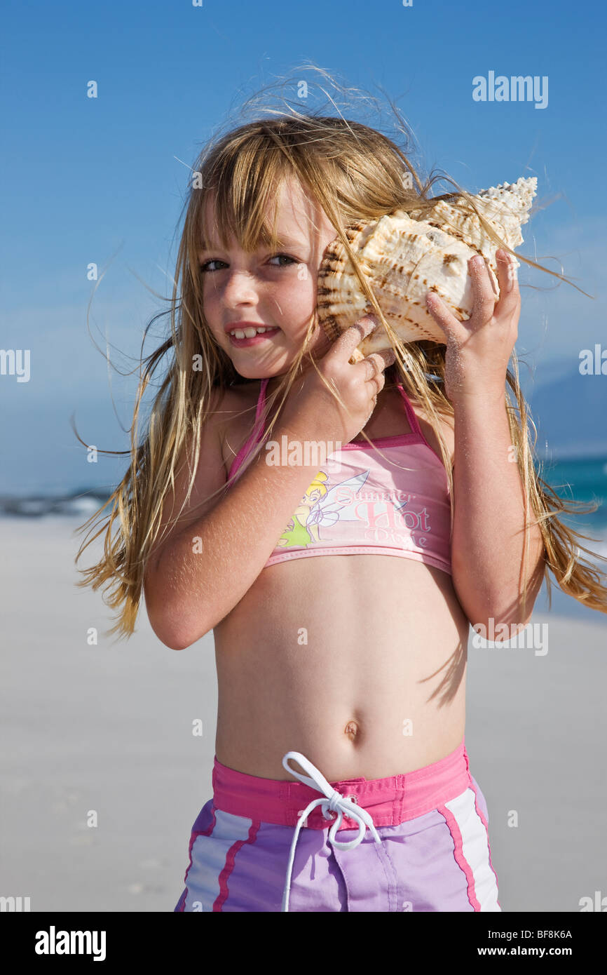 Cute Little Girl celebración shell para oreja en la playa. Cape Town South Africa Foto de stock