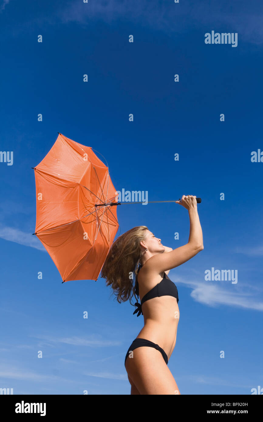 Mujer sosteniendo inside out paraguas naranja contra el cielo azul Foto de stock