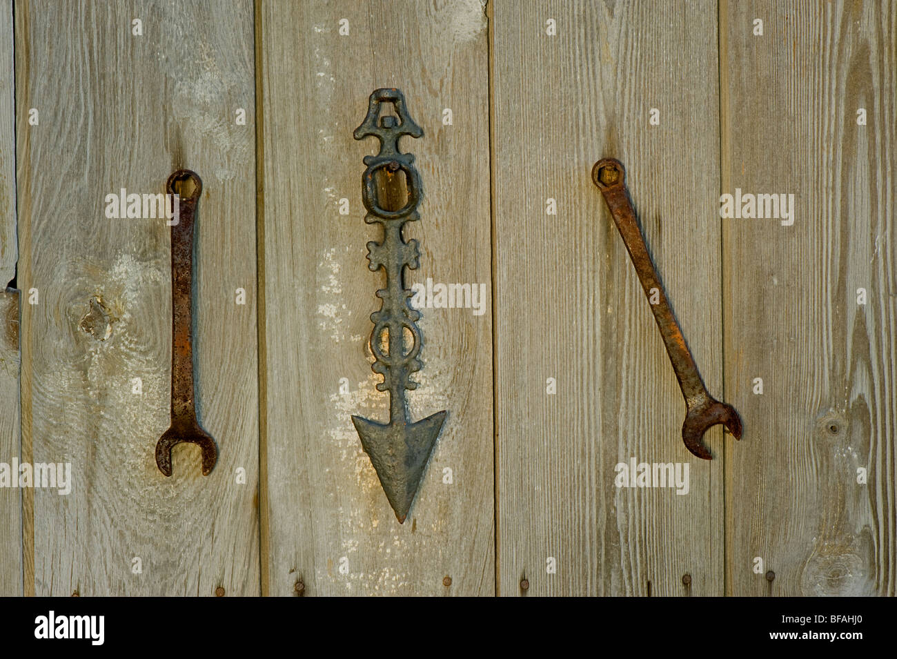 Dos llaves y una flecha colgando de un viejo cobertizo. Una de las llaves sigue la dirección de la flecha y el otro no. Foto de stock