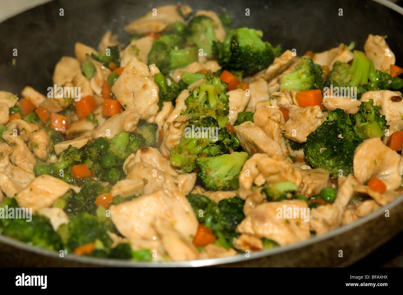 Pollo y brócoli salteado comida. Cerca, en la sartén, cocinar, pollo, zanahorias, guisantes, brócoli, salsa, caliente y humeante. Foto de stock