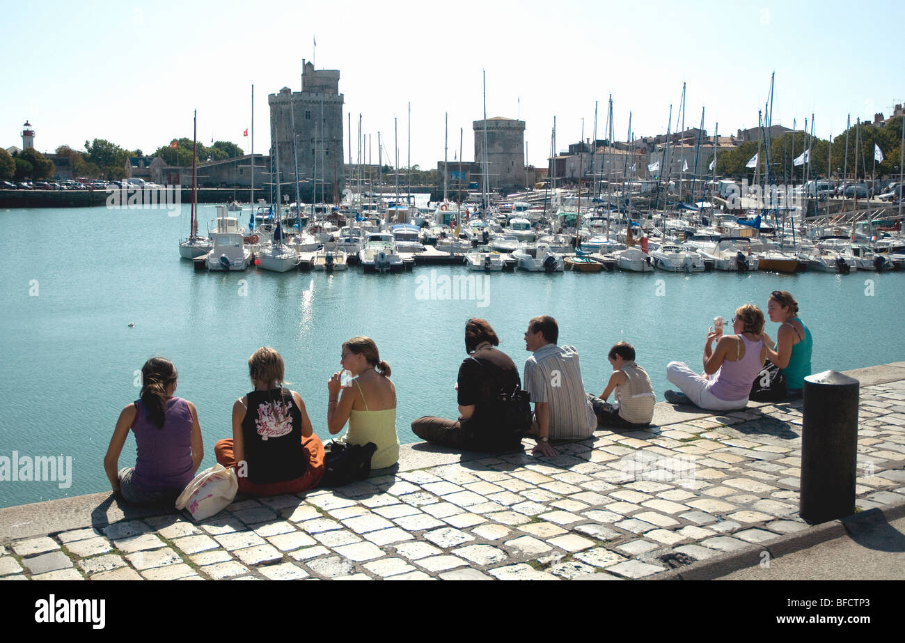 Los jóvenes sentados en el muro del puerto alto sobre el agua disfrutando de la vista del Viejo Puerto de La Rochelle Foto de stock