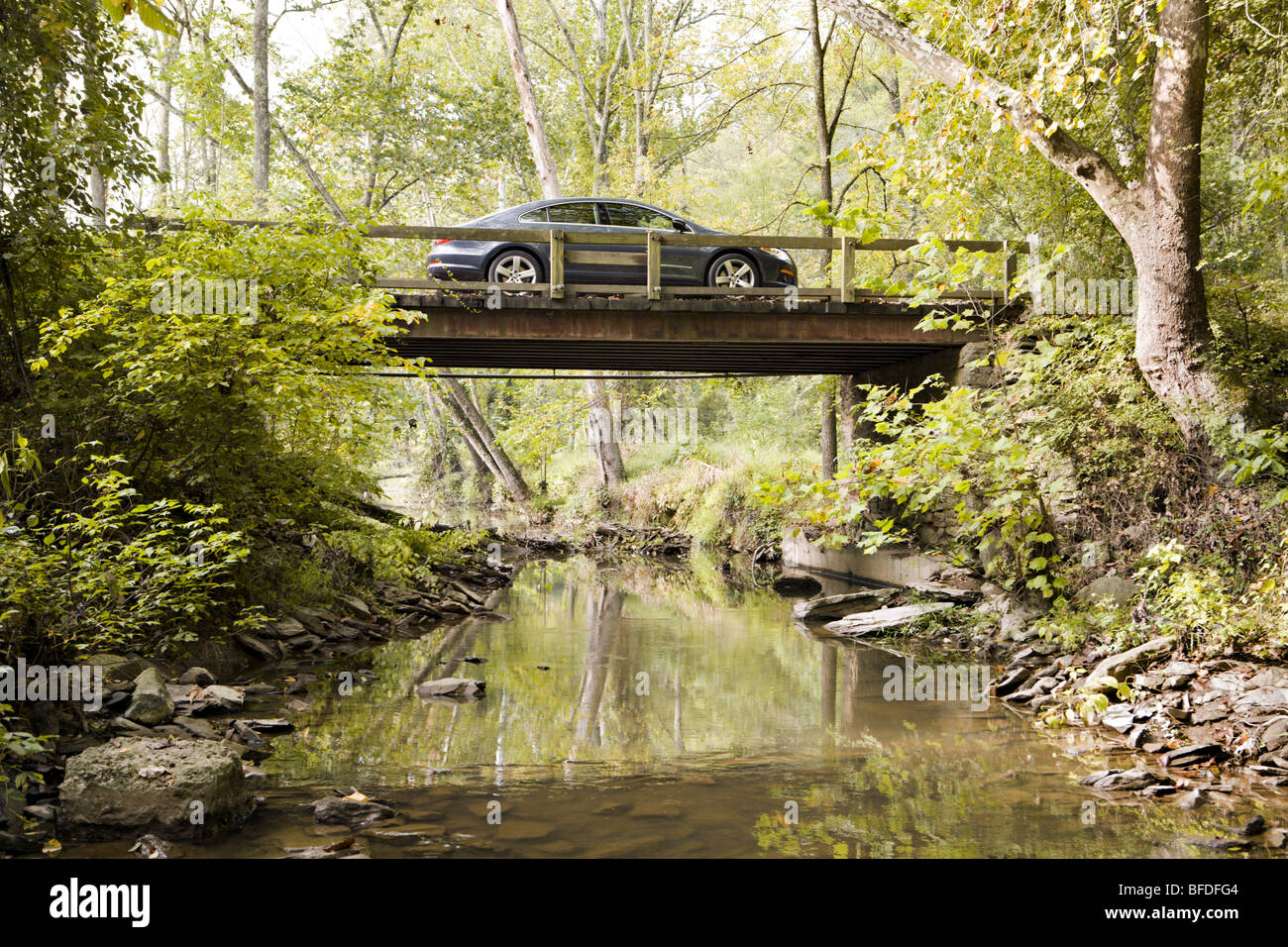 Un nuevo coche sobre un puente de madera en un paisaje forestal rural. Foto de stock