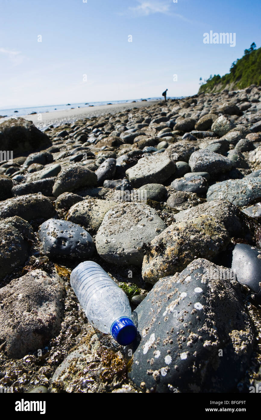 Un solo uso descarta una botella de agua de plástico transparente en una costa rocosa. Foto de stock