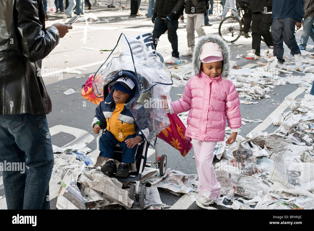 Negro guapo infante en cochecito y su hermana chicas en rosa, ambos vistiendo gorras de los Yankees de Nueva York, parecen desconcertados por trozos de papel en calle Foto de stock