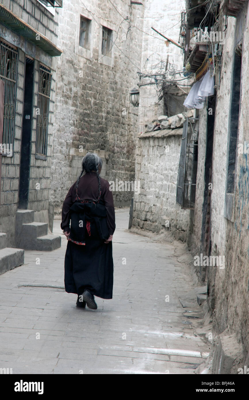 Old mujer tibetana caminando por las calles de atrás de la zona del casco antiguo de la ciudad de Lhasa Foto de stock