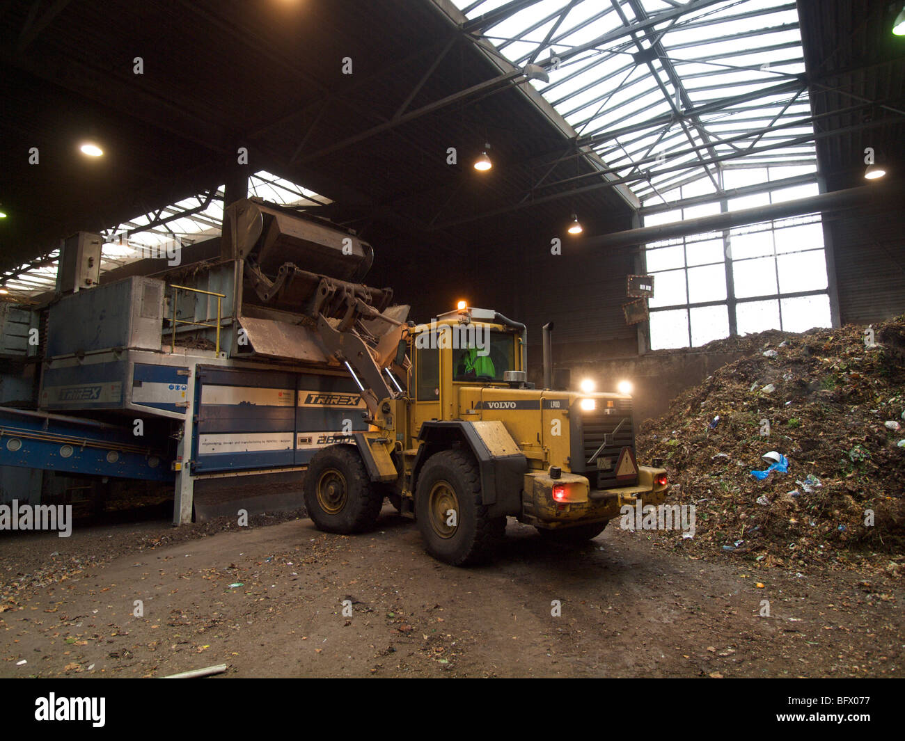 Pala de carga de desechos de materiales naturales en gran trituradora en la planta de compostaje, donde serán procesados para convertirse en biomasa Foto de stock