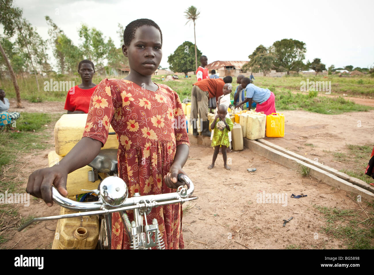 Una niña transporta agua desde un pozo con su bicicleta en la localidad de Amuria en el noreste de Uganda. Foto de stock