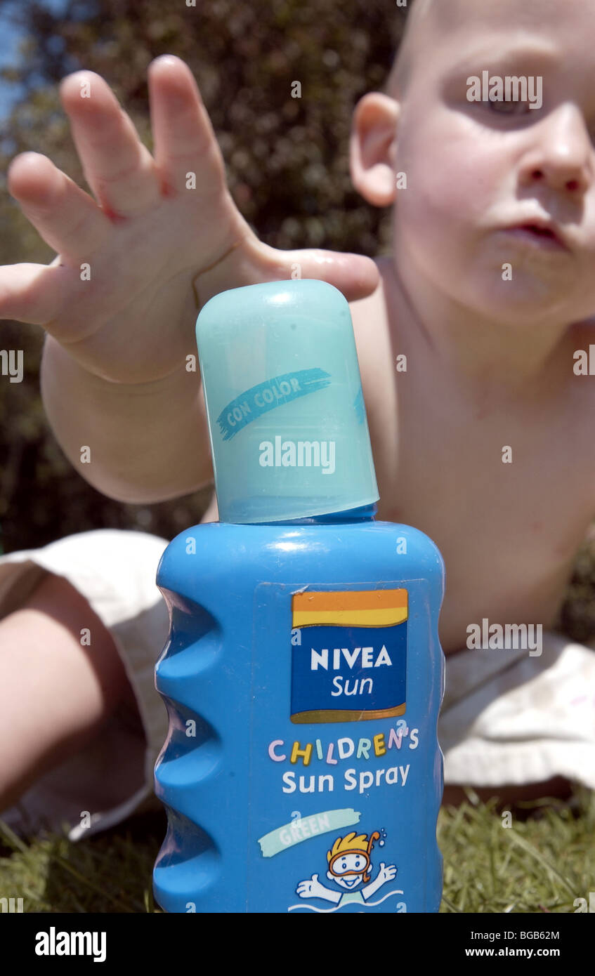 Bebé llegar a agarrar una botella de crema solar Foto de stock