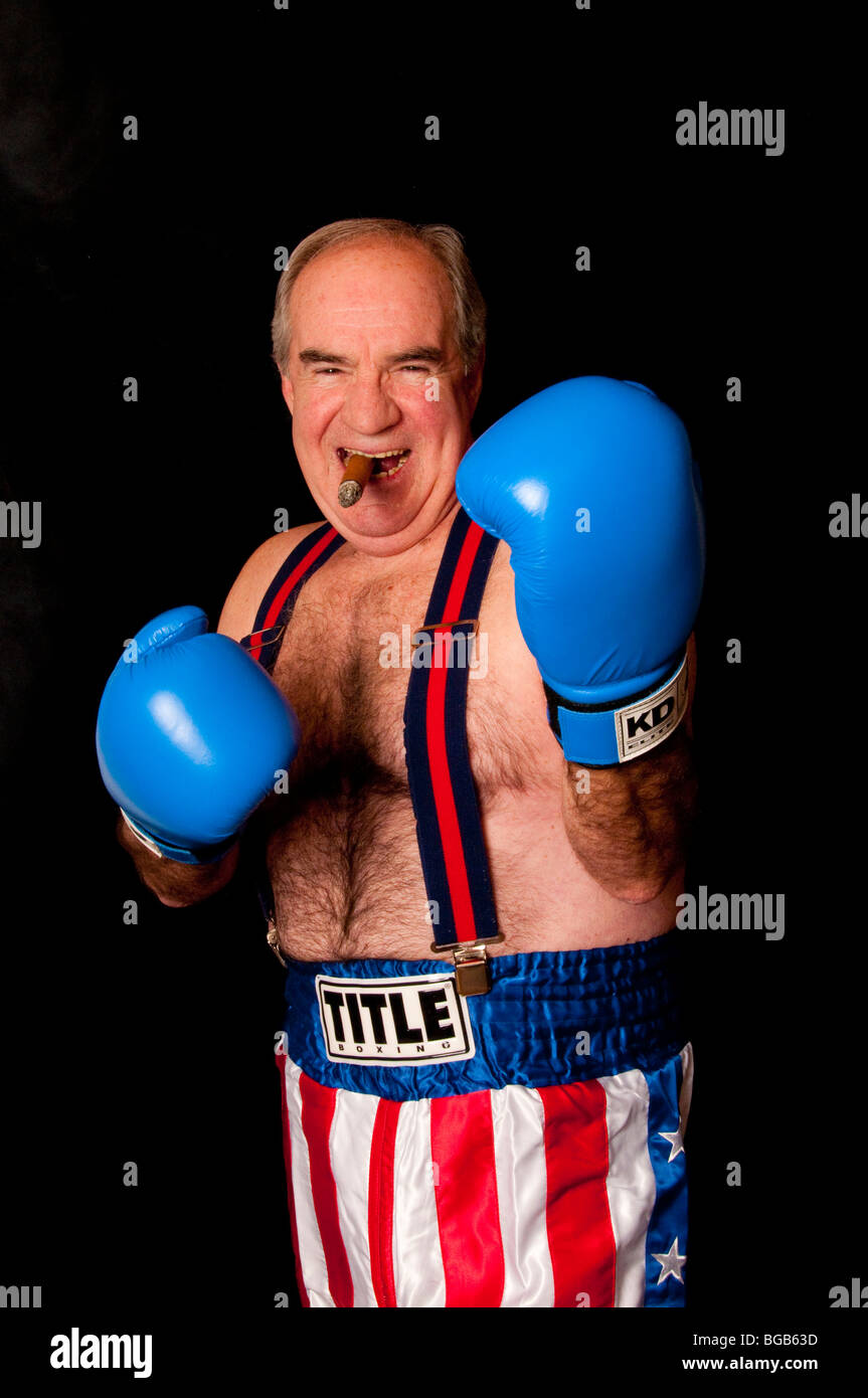 Envejecimiento boxer sobre fondo negro con bandera americana boxer troncos, guantes azules y tirantes fumar un cigarro Foto de stock