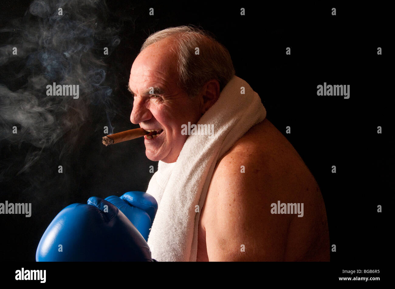 Perfil de envejecimiento boxer con cigarro y la sonrisa en la cara. Toalla alrededor de cuello azul con guantes de boxeo en posición de combate. Foto de stock