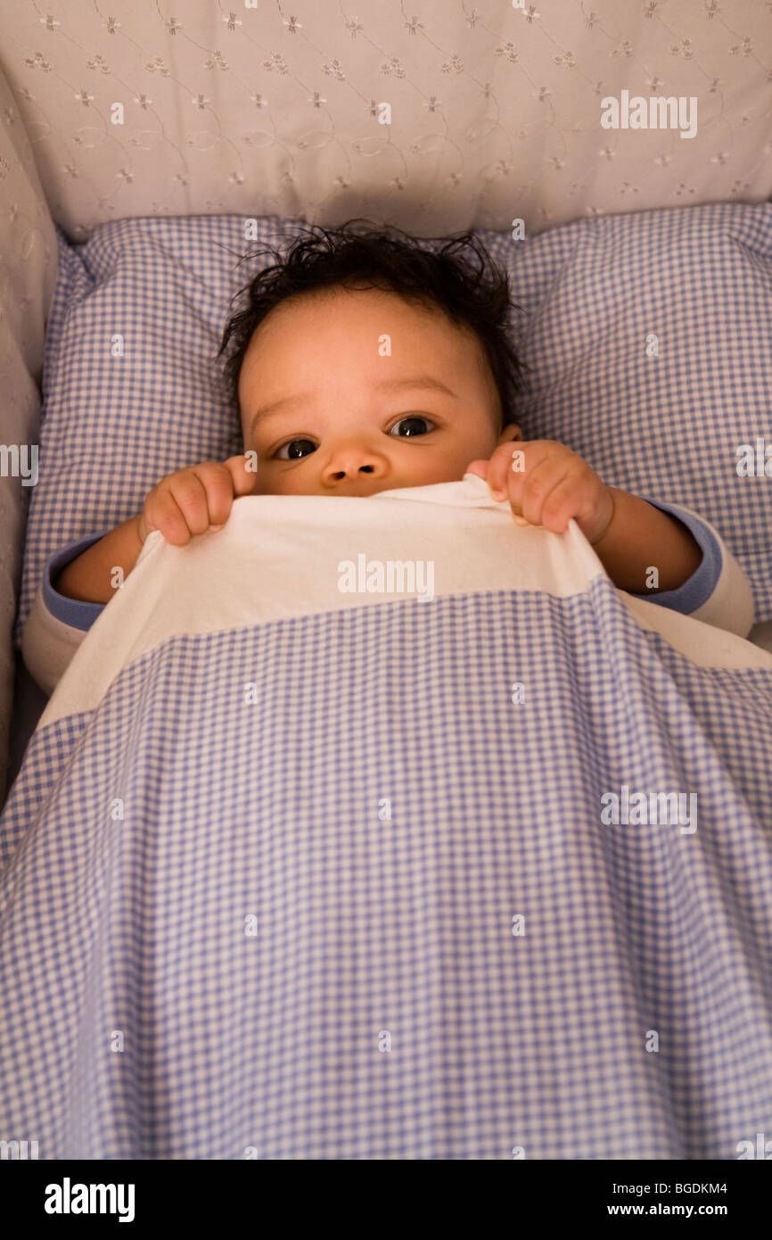 3 1/2 meses niño acostado en su cama y esconderse bajo su edredón. Foto de stock