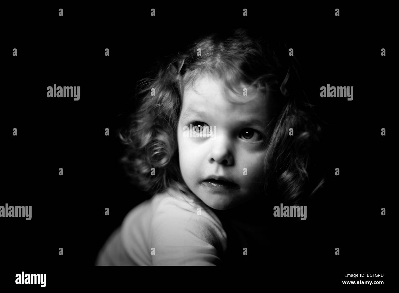 Fotografía en blanco y negro de una niña de tres años en una iluminación espectacular. Fondo negro. Foto de stock
