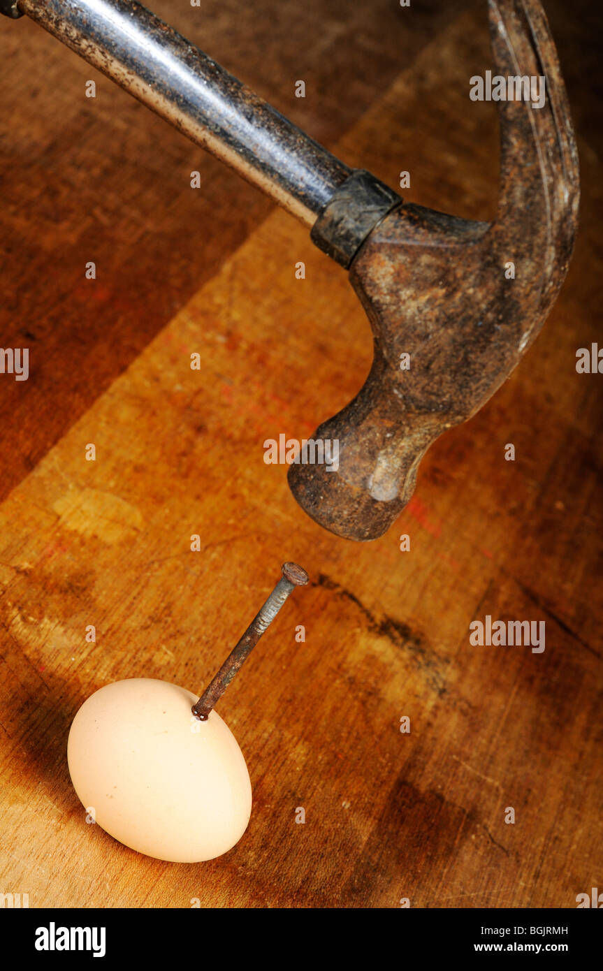 Fotografía de Stock de un clavo está siendo martillar en un huevo en una mesa de madera. Foto de stock