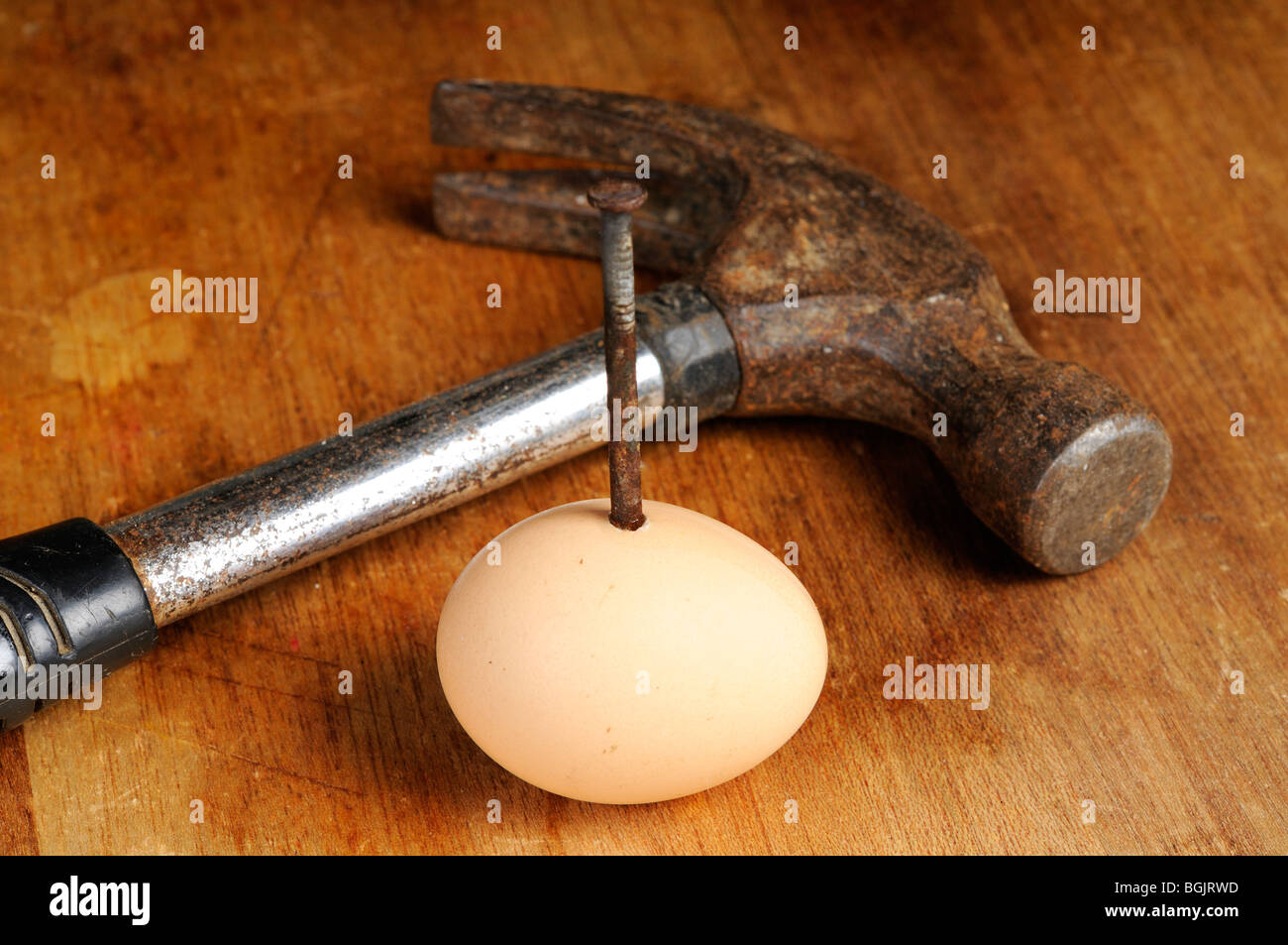 Fotografía de Stock de un clavo oxidado clavados a través de un huevo. Un viejo martillo está tumbado junto al huevo. Foto de stock