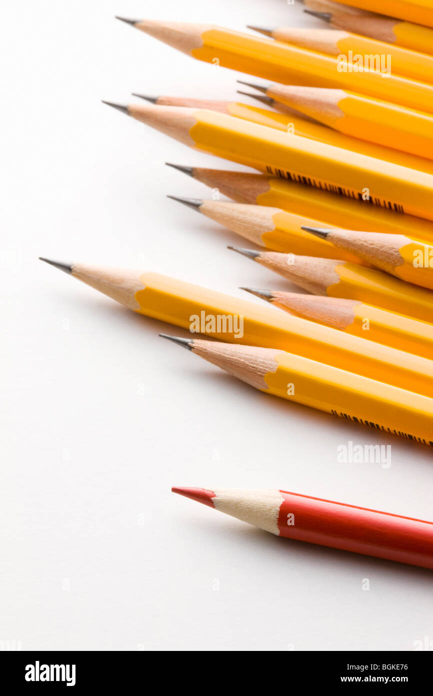 Lápiz rojo sobresaliendo del grupo de lápices de color amarillo Foto de stock