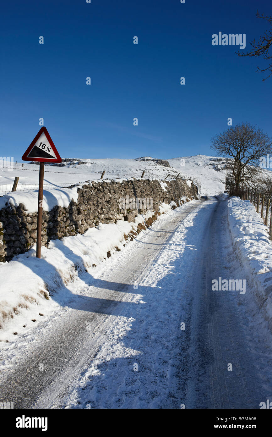 Un helado, la nieve cubrió el 16% de carretera con un signo de advertencia de gradiente Foto de stock