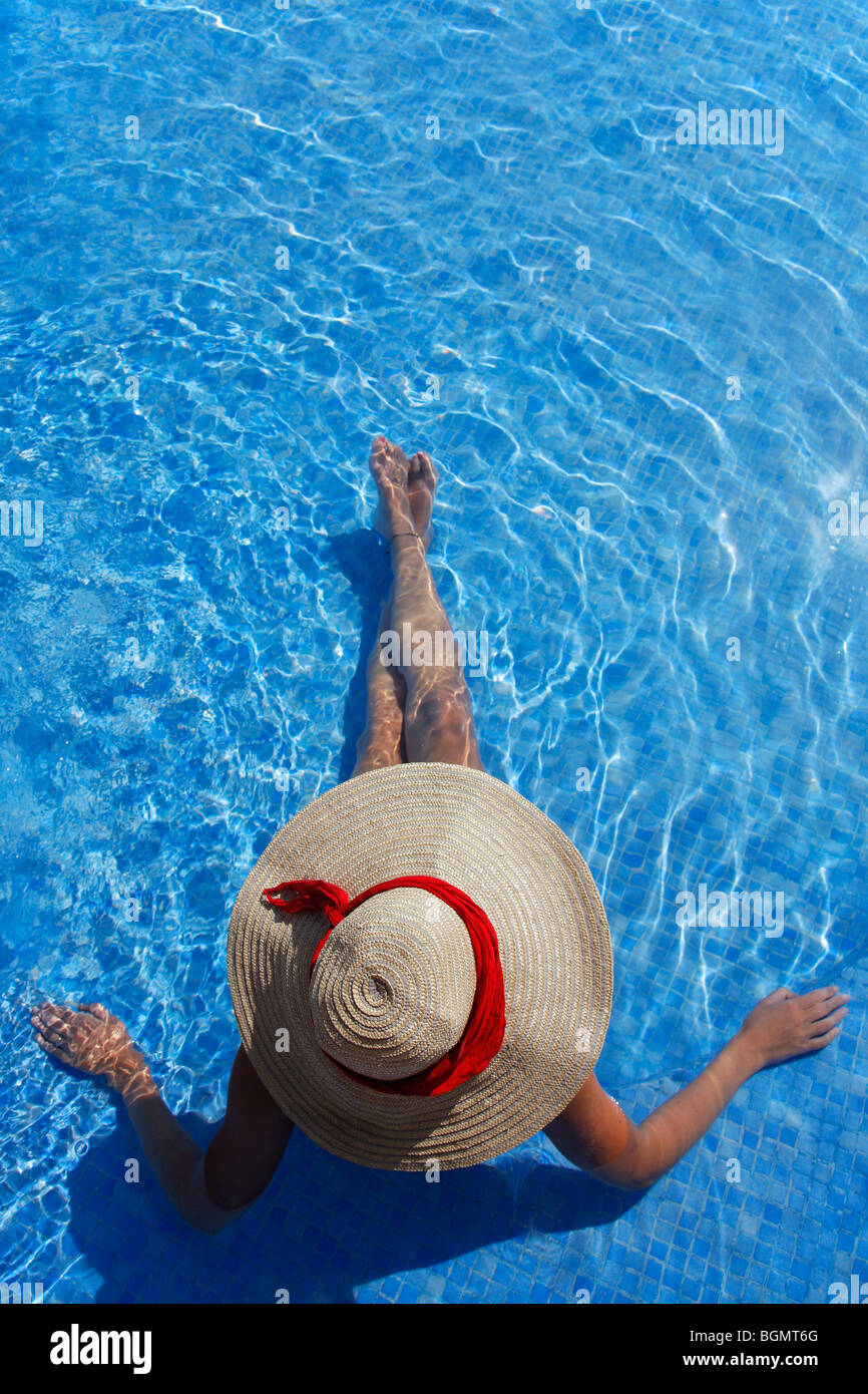 Mujer en un sombrero para el sol tomar el sol en una piscina de color azul Foto de stock