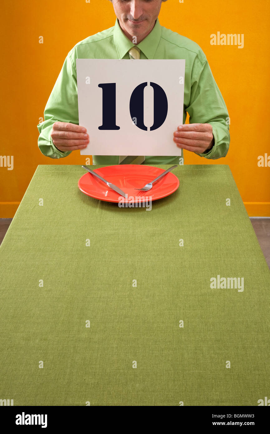 Hombre comiendo en la mesa mantiene 10 firmar para calificar la cena Foto de stock