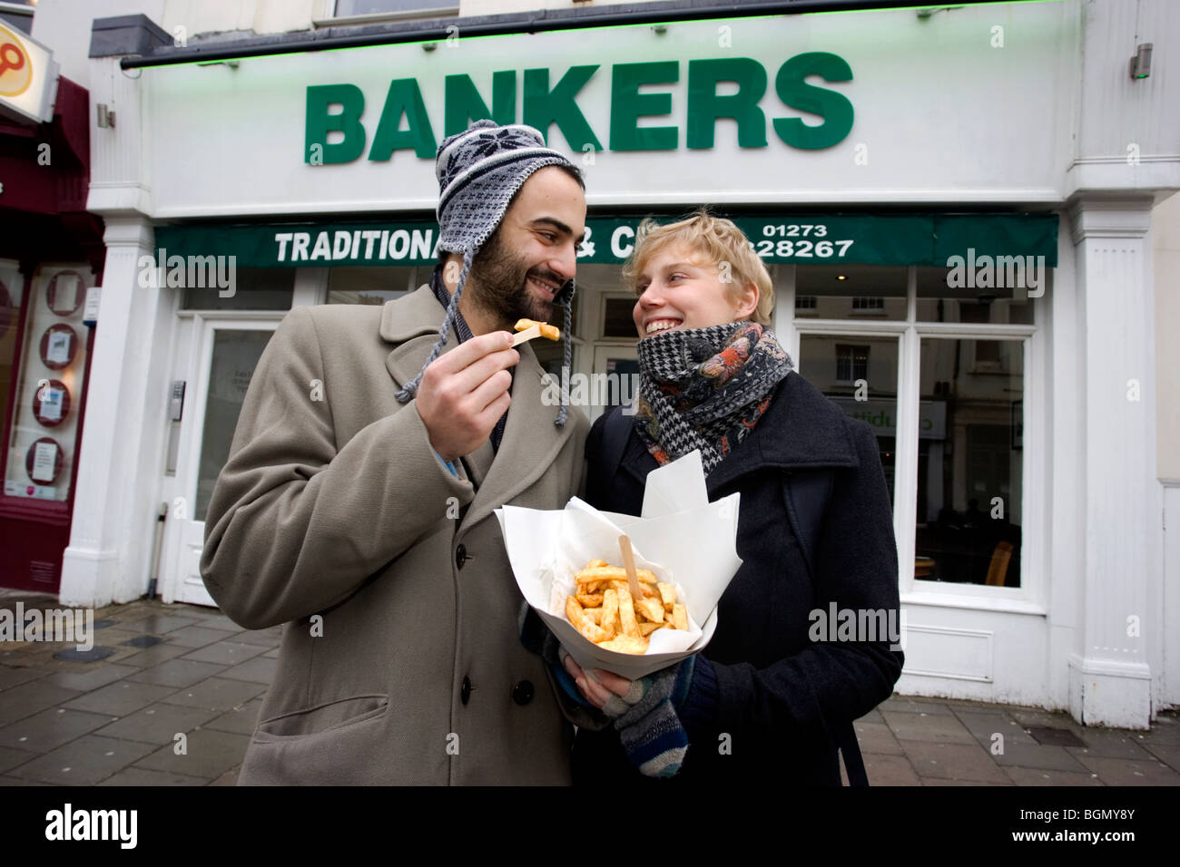 Una joven pareja disfrute de una pequeña porción de fichas fuera de banqueros tradicional restaurante fish and chips y take-away, Brighton, Reino Unido. Foto de stock