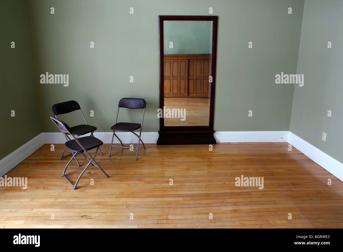 Habitación Vacía, tres sillas plegables, espejo, pisos de madera Foto de stock